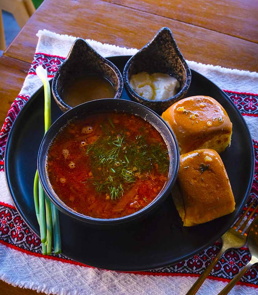 Ukrainian borshch with sour cream and dill garnish, served with garlic buns at Oasis Food